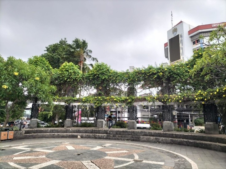 Area Landmark melingkar di Taman Pandanaran Semarang dengan pergola tanaman bunga kuning yang asri, berlatar belakang gedung perkotaan di pusat Kota Semarang.