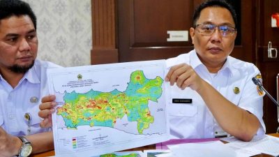 Kepala Dinas ESDM Jawa Tengah, Agus Sugiharto (kanan), yang mengenakan kemeja putih dan berkacamata, memegang dan menunjukkan "Peta Zona Kerentanan Gerakan Tanah Provinsi Jawa Tengah" yang menampilkan area berwarna merah, kuning, dan hijau. Ia didampingi seorang pria lain di sebelah kiri yang juga melihat ke arah peta tersebut dalam sebuah ruangan kantor.