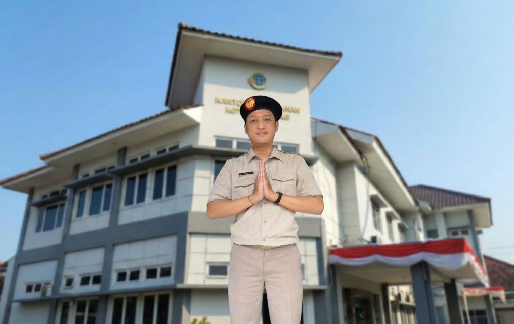 Seorang pegawai pria berseragam khaki dan berpeci hitam melakukan salam dengan tangan ditangkupkan di depan gedung Kantor Pertanahan Kota Semarang di bawah langit biru yang cerah.