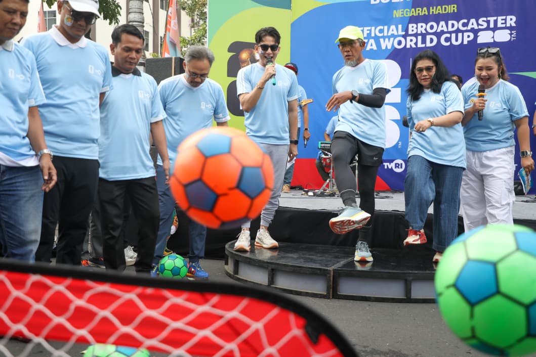 Sekretaris Daerah (Sekda) Provinsi Jawa Tengah, Sumarno, yang mengenakan topi kuning, celana hitam, dan kaus biru muda seragam TVRI, sedang menendang bola sepak berwarna oranye-biru ke arah gawang mini di atas panggung. Ia dikelilingi oleh beberapa orang lain yang tersenyum, termasuk pembawa acara yang memegang mikrofon. Latar belakang panggung menampilkan spanduk besar bertuliskan "OFFICIAL BROADCASTER PIALA WORLD CUP 2026" dan logo TVRI.