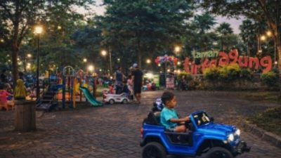 Anak bermain mobil mainan di Taman Tirto Agung Banyumanik saat sore hari dengan latar playground, pepohonan rindang, dan suasana taman kota Semarang.
