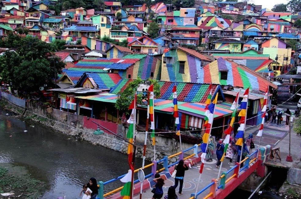 Pemandangan deretan rumah warna-warni di lereng bukit Kampung Pelangi Semarang beserta jembatan ikonik di atas sungai.
